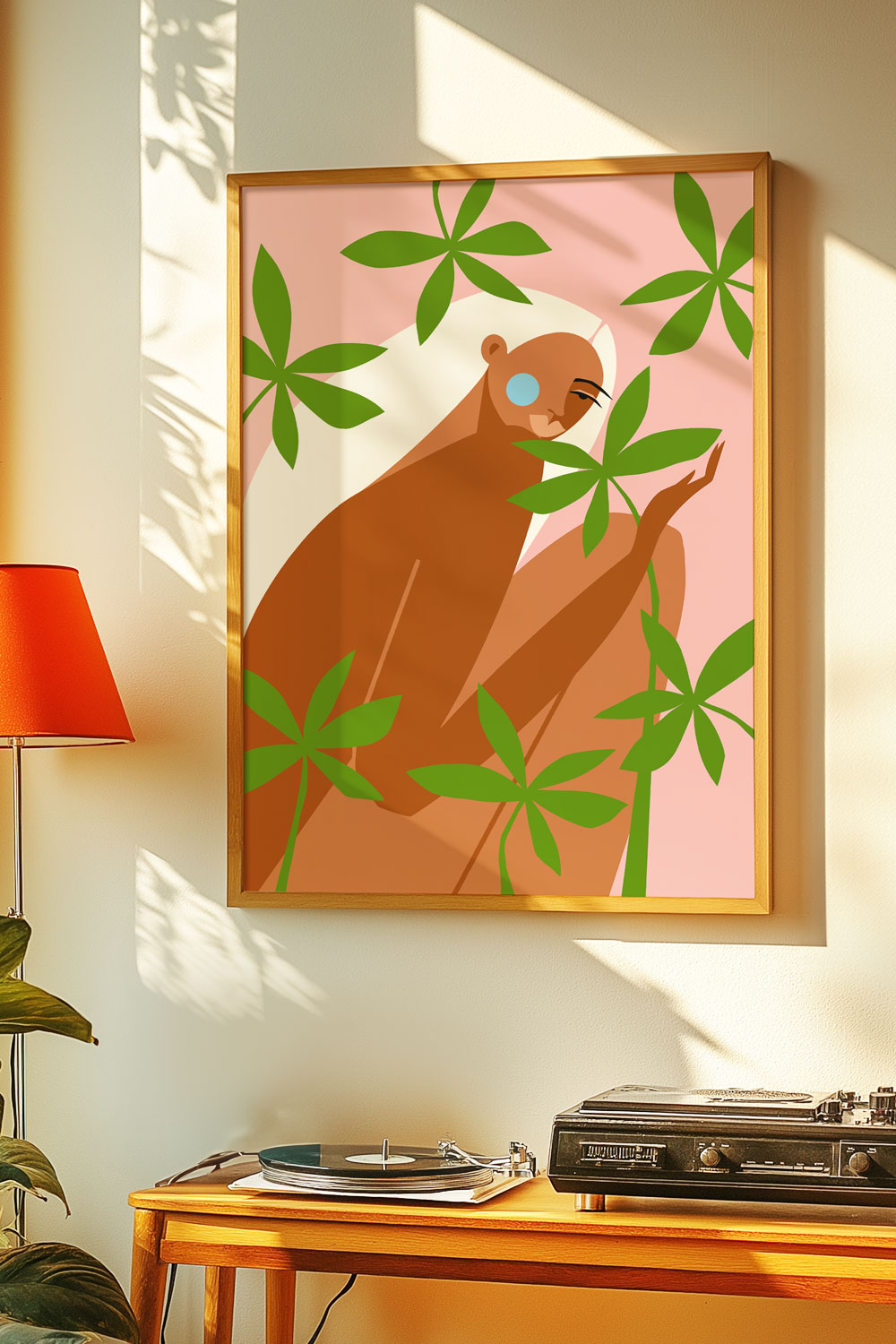 Framed illustration of a nude figure surrounded by green leaves, displayed above a vintage record player and styled with warm natural light.